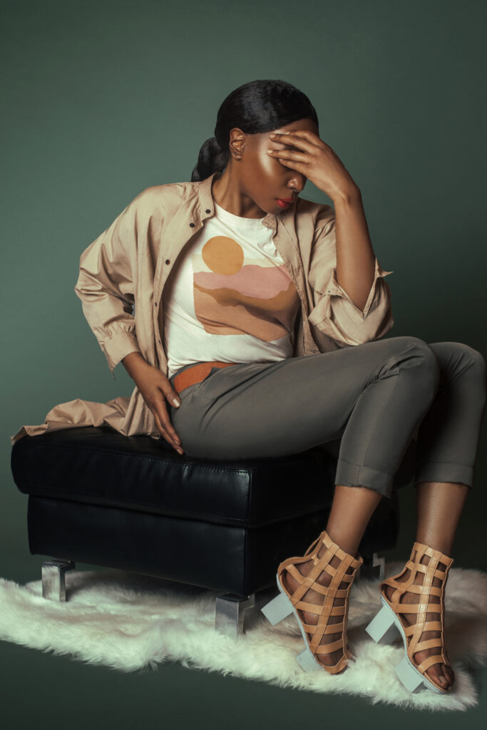 Summer sandals for women. An elegant Back woman siting on a couch wearing brown sandals.