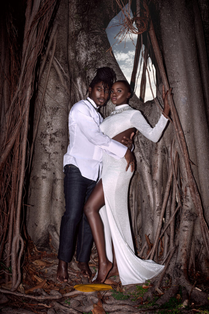 Day Rates for Photographers. Portrait of a sexy Millennial black couple posing by themselves outside barefoot leaning on an old oak tree on a summer day wearing jeans, long sleeve shirt and a long white dress with jewelry.