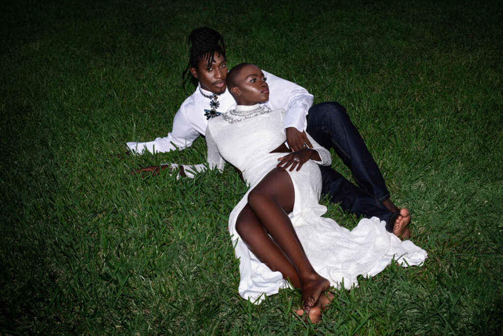 Day Rates for Photographers. Portrait of a Millennial black couple posing by themselves outside laying on grass barefoot on a summer evening wearing jeans, long sleeve shirt and a long white dress with jewelry.
