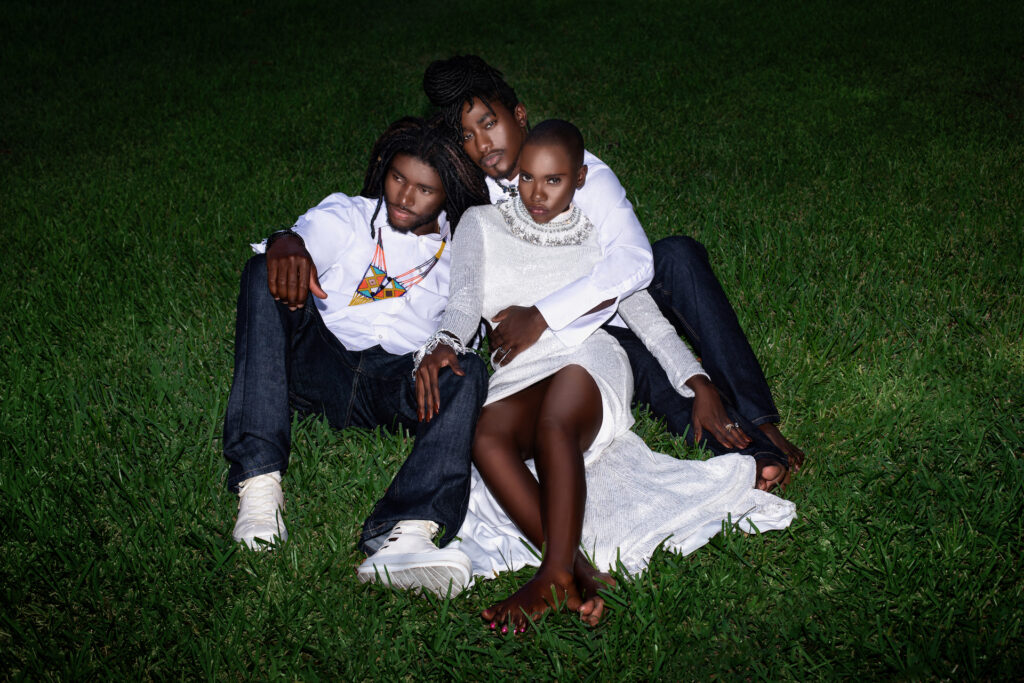 Day Rates for Photographers. Portrait of a group of Millennial black people posing by themselves outside sitting on grass on a summer evening wearing jeans, long sleeve shirts with sneakers and a long white dress with jewelry.