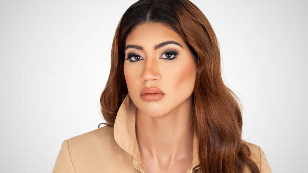 Become your own best friend. Closeup portrait of a sexy young Latina with long wavy hair and beautiful makeup sitting inside a studio wearing a beige trench coat.