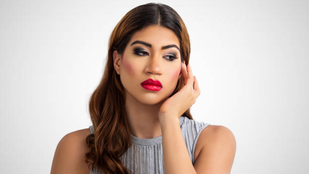 Become your own best friend. Closeup portrait of a serene young Latina with long wavy hair over her left shoulder, perfect eye brows, dark eye makeup and red lipstick wearing a grey bare shoulder dress.