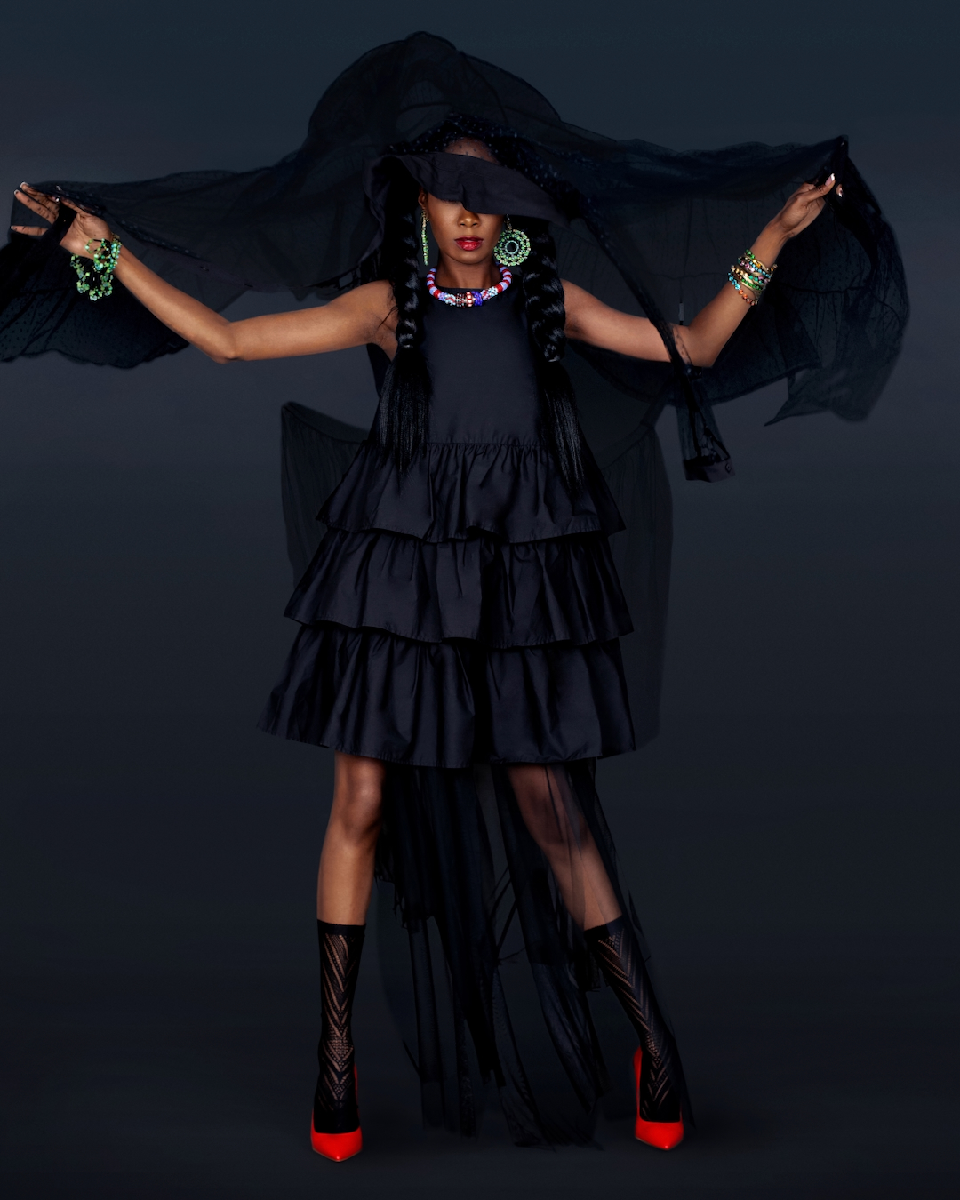 Model Maria wearing a flowing black dress, red platform shoes and statement jewelry in the Let It Flow fashion editorial