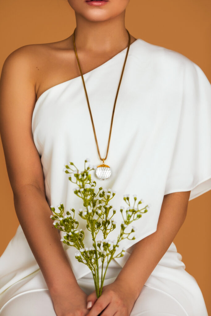 Closeup portrait of a lovely Latin girl with beautiful makeup posing by herself inside a studio with pecan color background wearing a white evening dress and beautiful necklace while holding flowers.