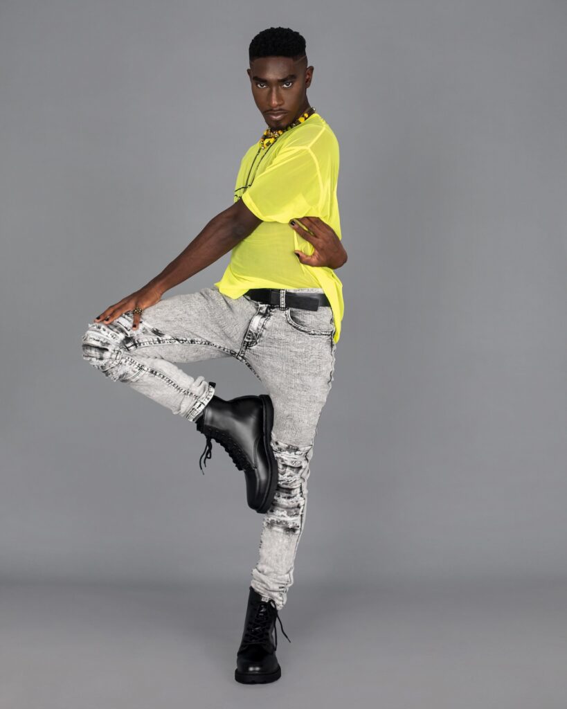 Handsome Black man wearing a yellow mesh top, grey jeans and black boots — Pretty Boy Joy editorial.