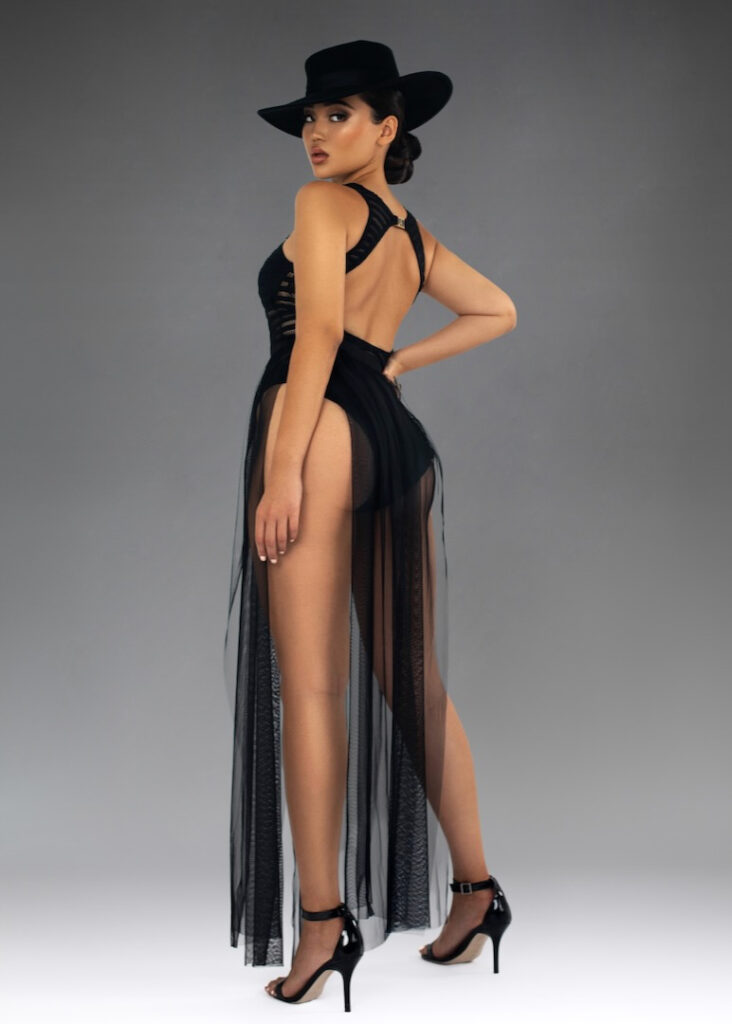 Crazy sexy confidence. Portrait of a confident young Asian woman with updo hair and beautiful makeup standing by herself inside a studio with a fading grey background wearing a black bathing suit, high heels and hat.