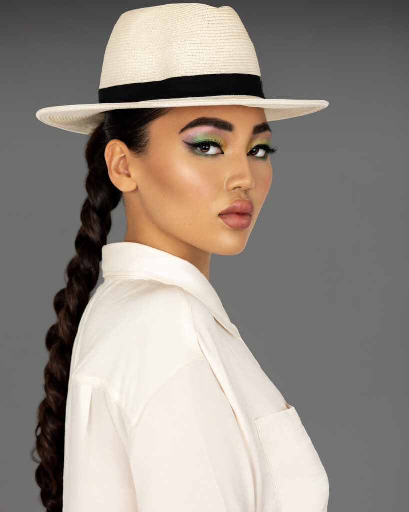 Crazy sexy confidence. Closeup portrait of a sensual young Asian woman with long braided ponytail hair and beautiful makeup standing by herself inside a studio with a grey background wearing a white fedora hat.