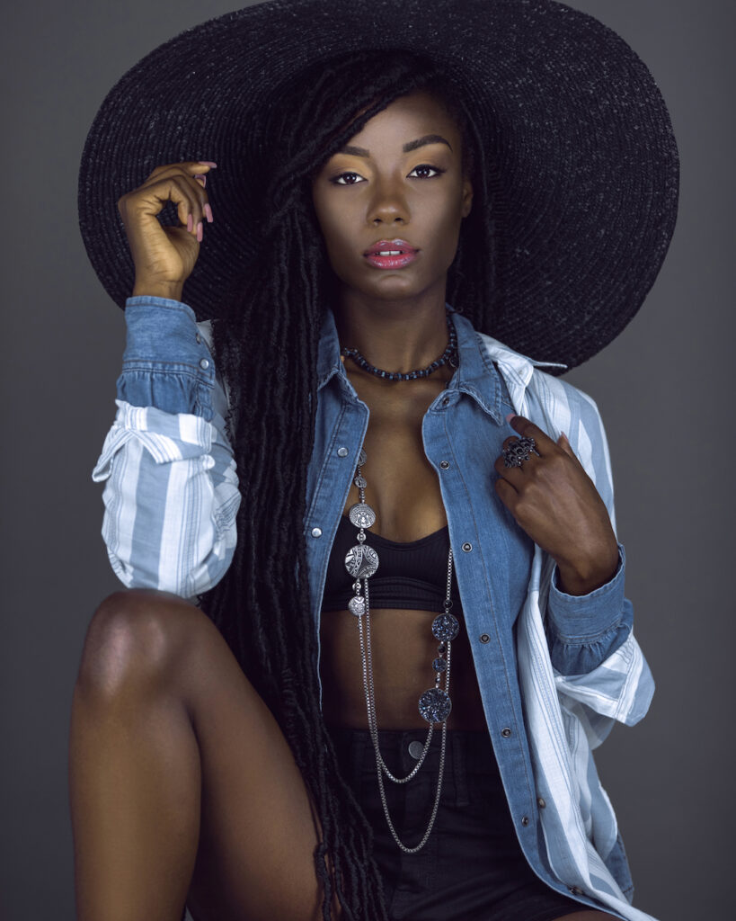 Locks of Beauty. Black female model with dreadlocks wearing striped shirt, jewelry, and summer hat in studio portrait.