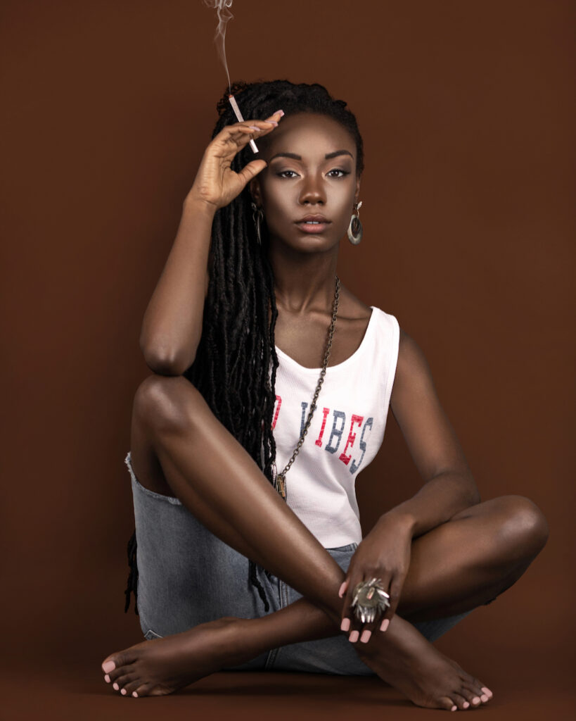 Locks of Beauty. Black female model with dreadlocks wearing summer outfit, sitting on floor against brown background.