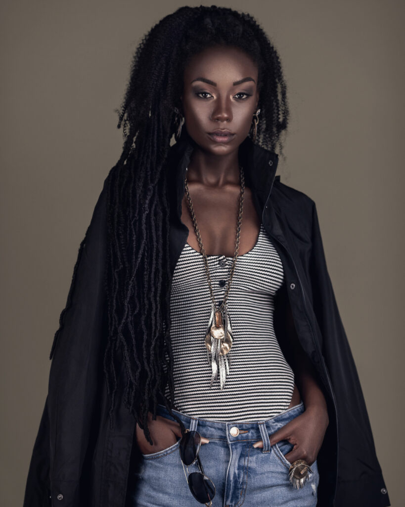 Locks of Beauty. Black female model with dreadlocks wearing denim shorts, jacket, and jewelry in studio.