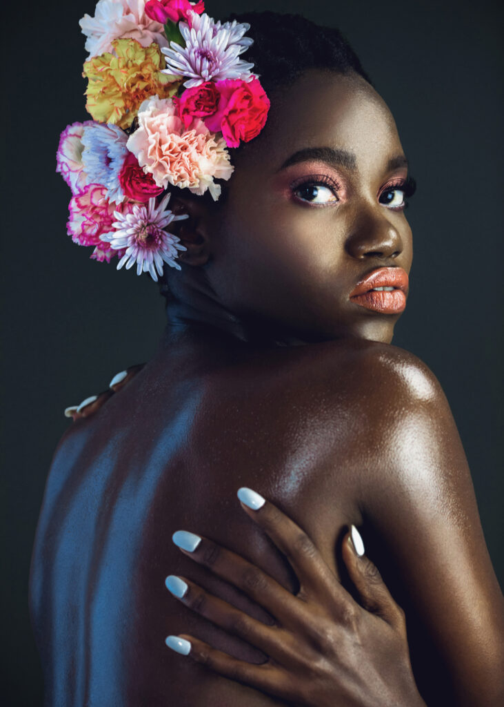 The Ethereal Goddess. Portrait of a sexy young black female with a short Afro, beautiful makeup and soft lips posing by herself in a studio with dark background wearing a bouquet of flowers in her hair.