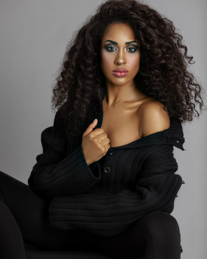 Portrait of confident Latin woman with curly hair in black wool sweater in studio for Curls Poppin.