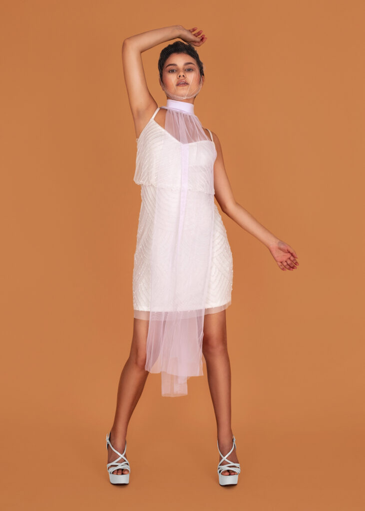 Portrait of a dancing Latin girl with long wavy hair in an up-do and beautiful makeup posing by herself inside a studio with a pecan color background wearing a white dress with high heels.