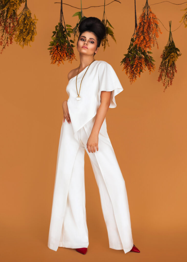 Latin model in white jumpsuit surrounded by flowers – fashion magazine editorial.