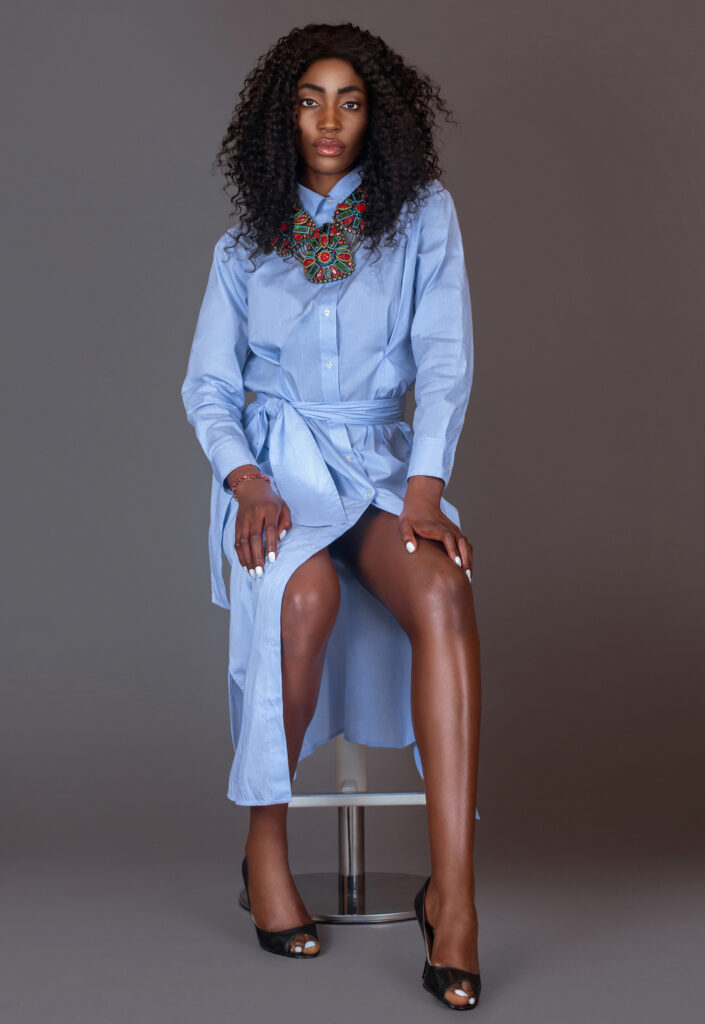 Spring Is In The Air. Black woman in blue dress with colorful jewelry sitting on fur in studio.