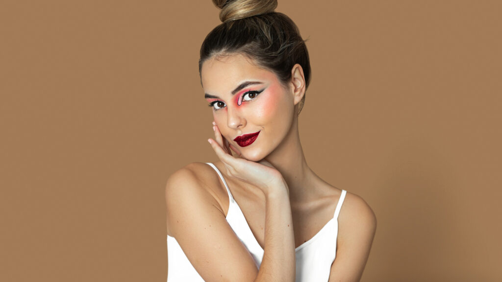 Modern beauty and self-expression. Manuella with long dark blond hair, eye makeup, white strap top, black skirt, studio with pecan background.