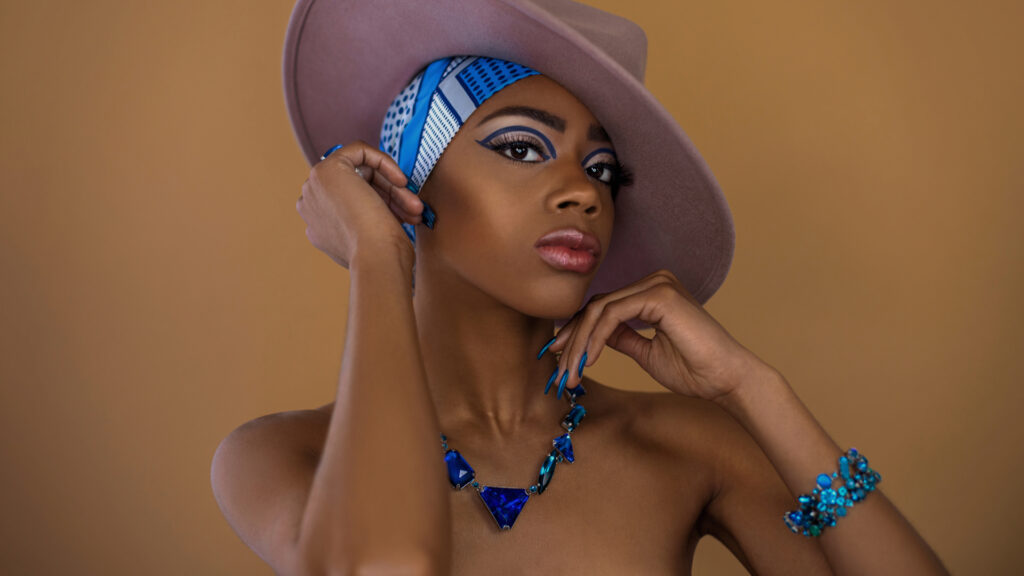 Gypsy Queens Editorial. Black model with a blue and white head scarf, grey hat, and blue Konplott jewelry