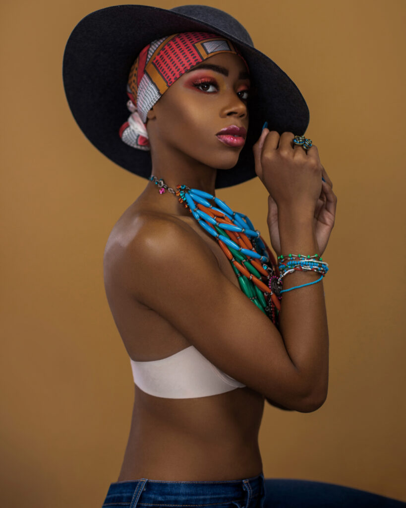 Gypsy Queens Editorial. Black model wearing a red and white head scarf, dark grey hat, and colorful jewelry