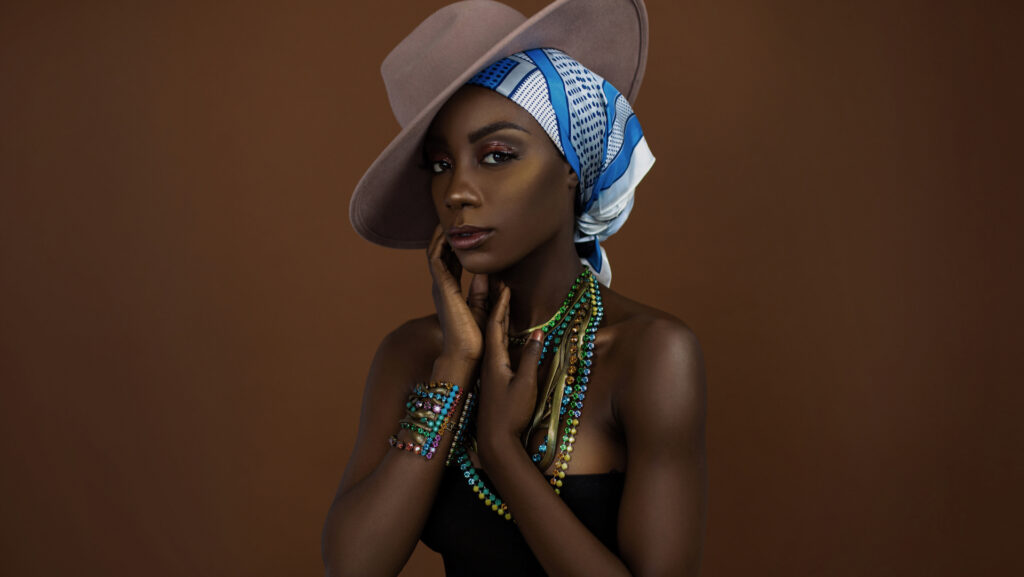 Gypsy Queens Editorial. Black model wearing a white and blue head scarf, beige hat, and colorful Konplott jewelry