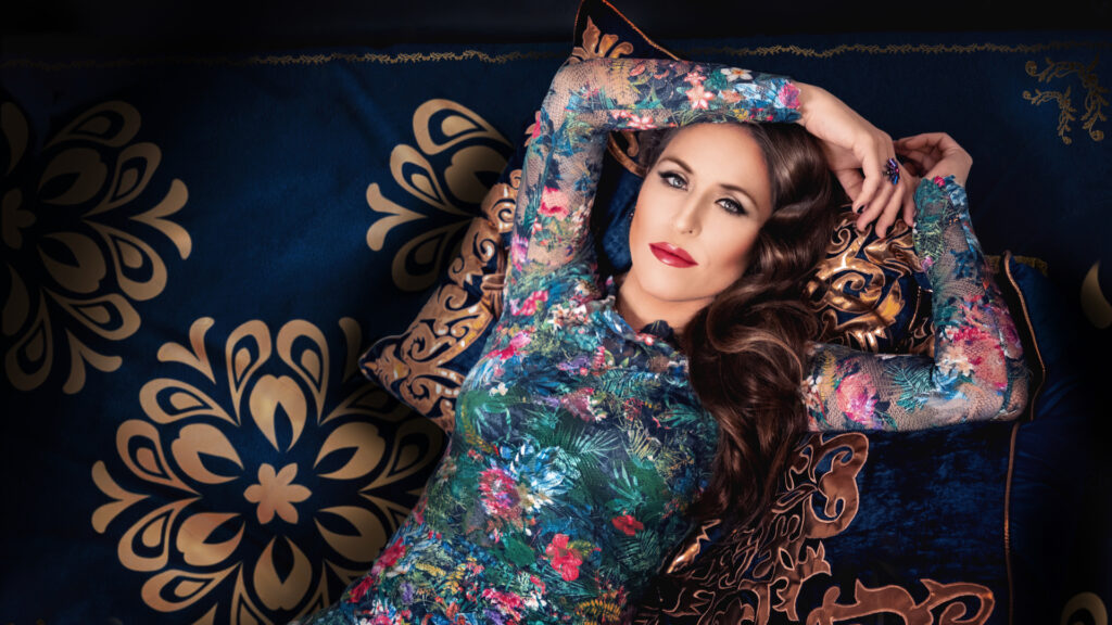 Britta Steffenhagen lying on a couch wearing a colorful evening dress and jewelry.