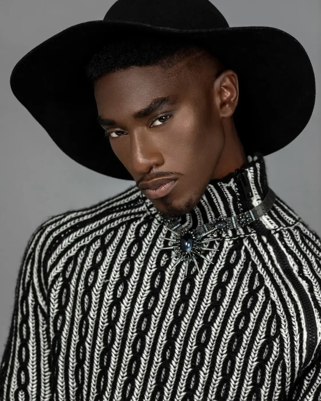 Black male model in a black-and-white sweater, hat and jewelry