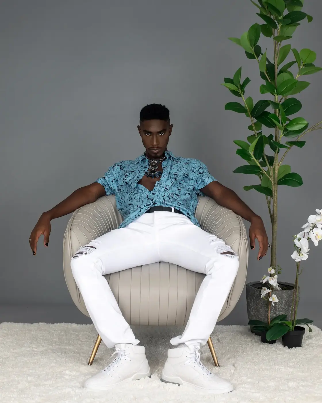 Relaxed seated portrait in a blue shirt, white trousers and jewelry