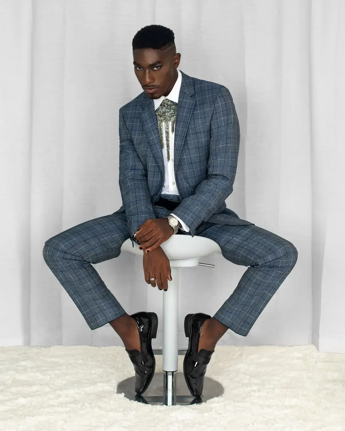 Black male model seated in a blue suit with statement jewelry