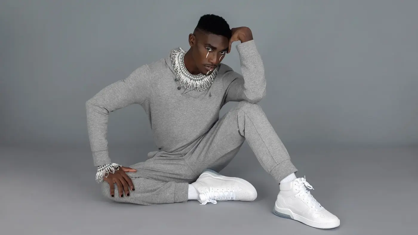 Black male model reclining in a grey tracksuit and white sneakers