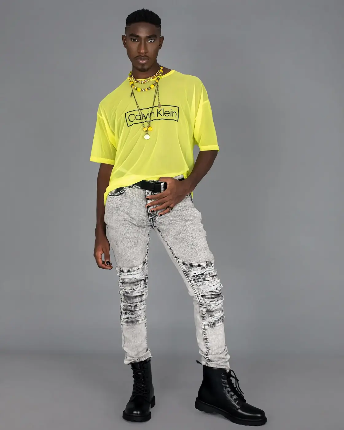 Black male model in a yellow mesh top, grey jeans and black boots