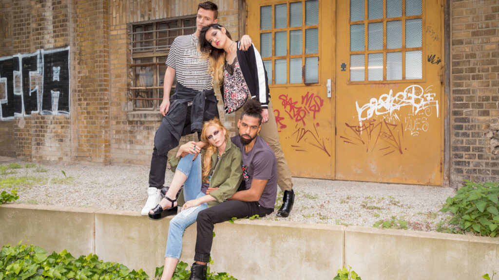 Group of four young adults posing by brick wall wearing Zadig & Voltaire outfits — Berlin fashion editorial.