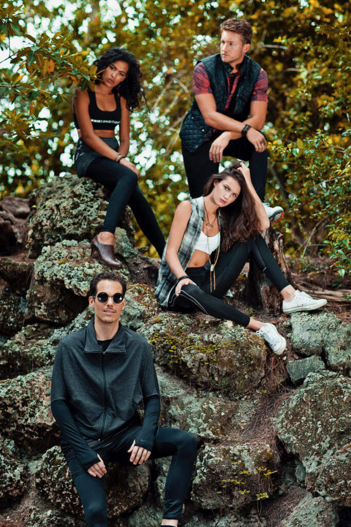 Urban fashion editorial portrait of diverse young adults sitting on a rock surrounded by trees wearing stylish urban outfits.