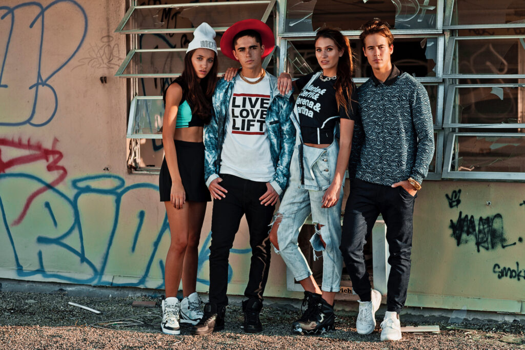 Confident group of young adults standing outdoors in Miami wearing modern street style outfits in front of a graffitied building.