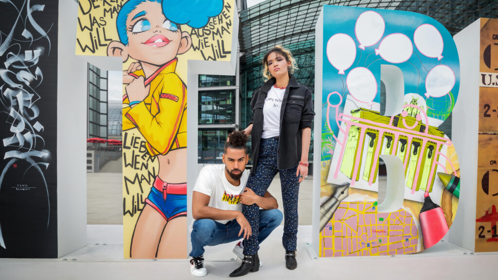Confident couple with natural hair standing before art pieces wearing Zadig & Voltaire outfits — Berlin fashion editorial.