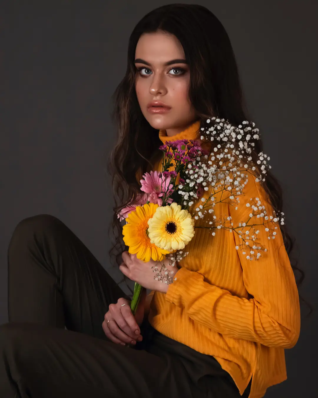 Female fashion model in an orange blouse holding colorful flowers in a studio portrait