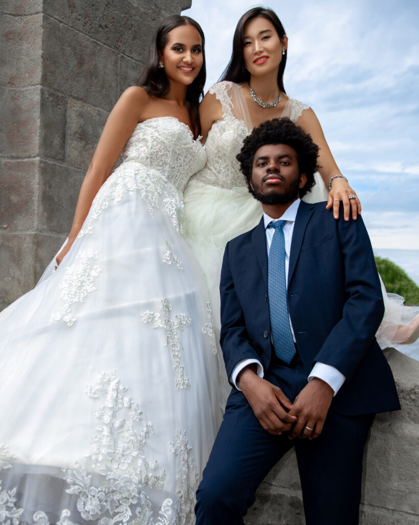 editorial wedding photography. Group portrait of one man and two women, dressed in wedding attire, standing in front of a concrete bridge.