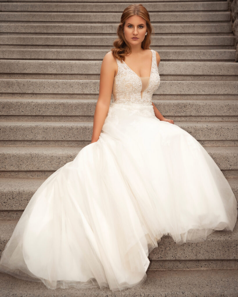 editorial wedding photography. Portrait of a white woman with long blonde hair sitting gracefully on concrete steps in a white wedding gown.