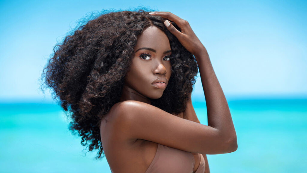 Young Black woman with long curly hair in brown bikini on tropical beach – beach fashion shoot