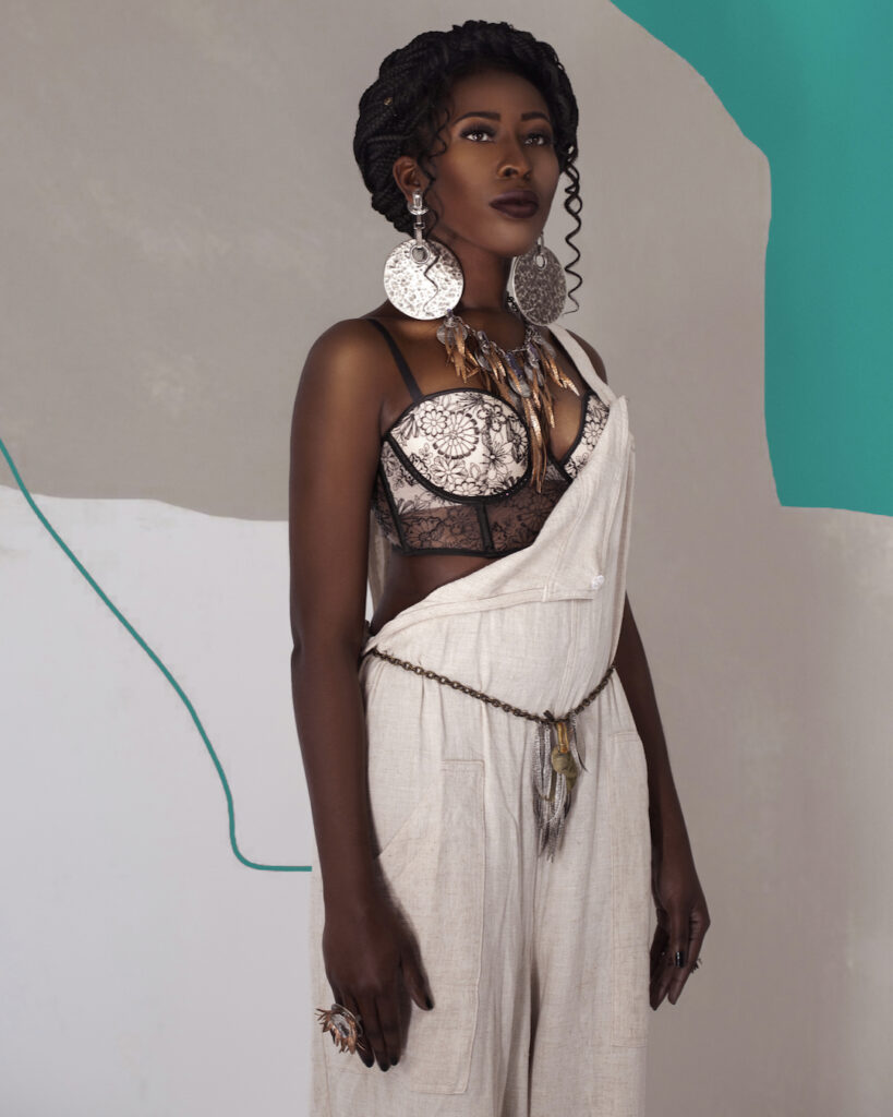 Artistic beauty photography portrait of a sexy young Black female with curly hair and bright jumpsuit in studio with silver jewelry.