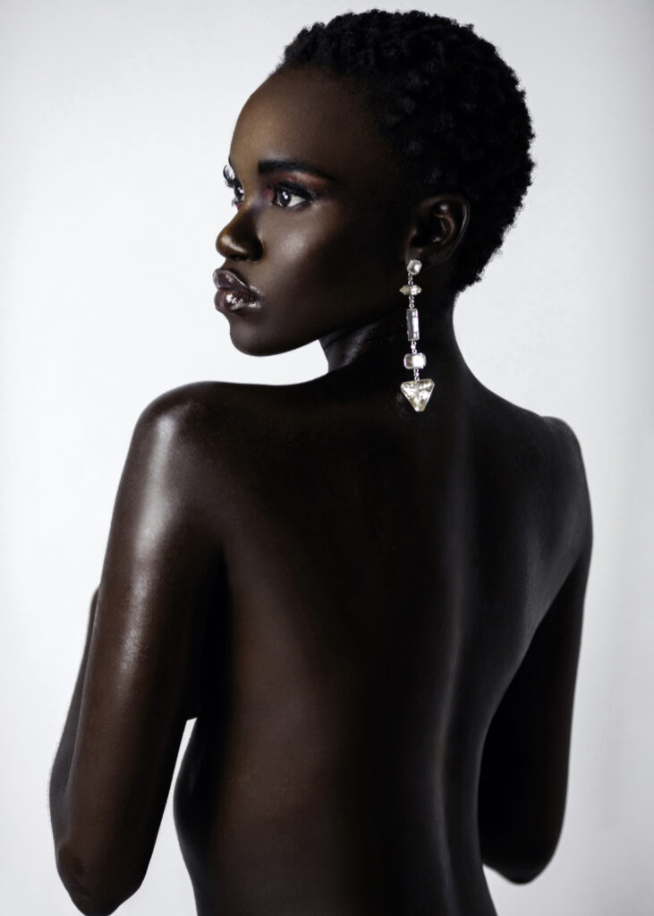 Beauty editorial close-up of young Black woman with short hair, moist lips, and diamond earrings against bright background.