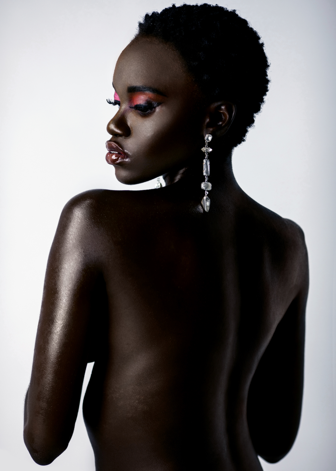 A portrait of a sexy young black female with short black hair and moist lip stick wearing a big diamond earring in front of a bright background.