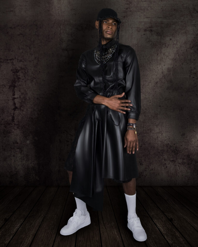 Avantgarde Fashion - portrait of a handsome Black man with silver jewelry and white sneakers in a dark studio background.
