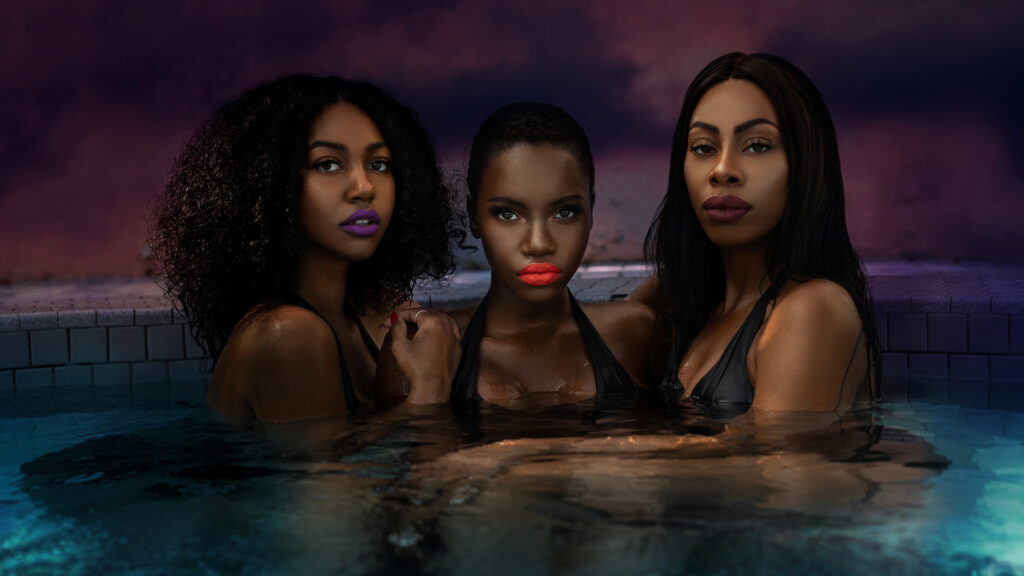 Artistic beauty photography portrait of three young Black females with bold lipsticks and manicured nails posing in a pool during the evening.