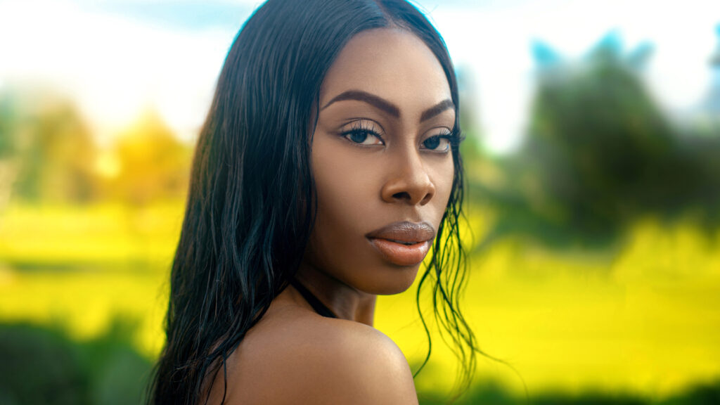 Closeup artistic beauty photography portrait of a young Black female’s face with luminous makeup and luscious lips in tropical surroundings.
