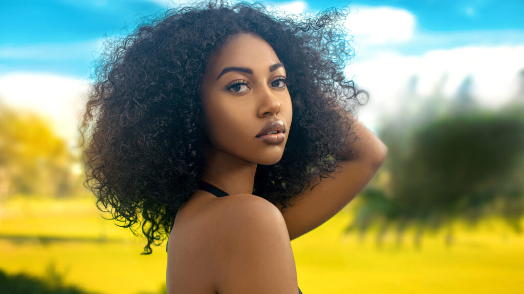 Closeup artistic beauty photography portrait of a serene young Black female with long curly hair in tropical surroundings wearing a black bikini top.