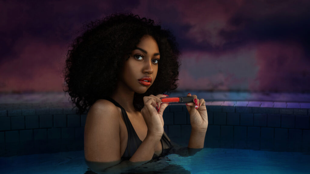 Artistic beauty photography portrait of a young Black female with curly hair holding a lipstick in a swimming pool.