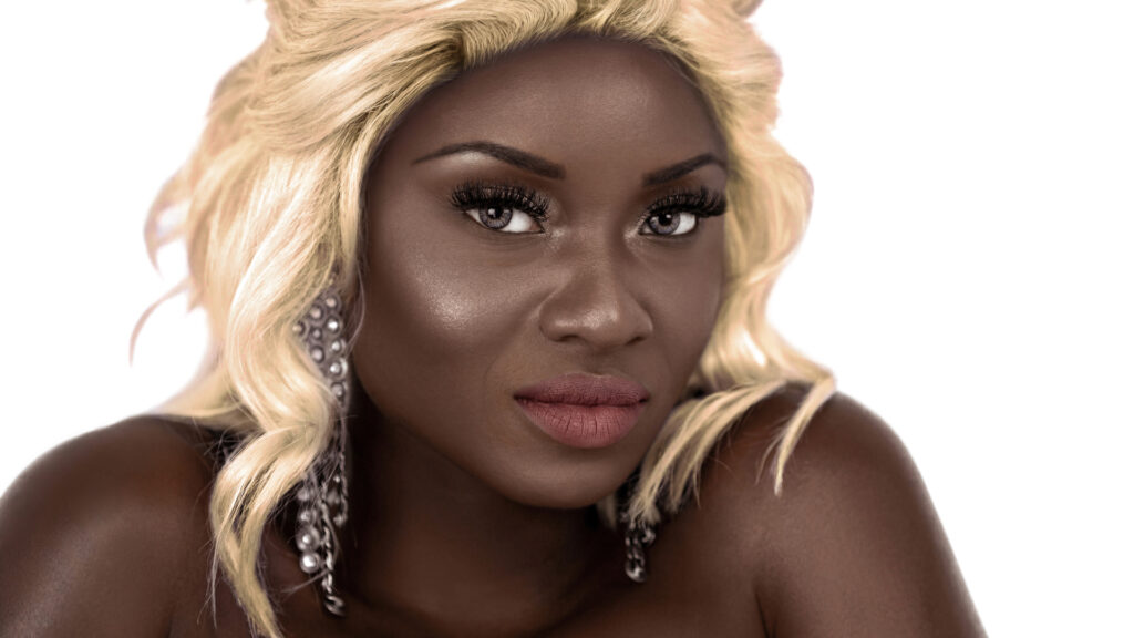 Headshot of a Black woman with blonde hair and silver jewelry in a white studio setting.