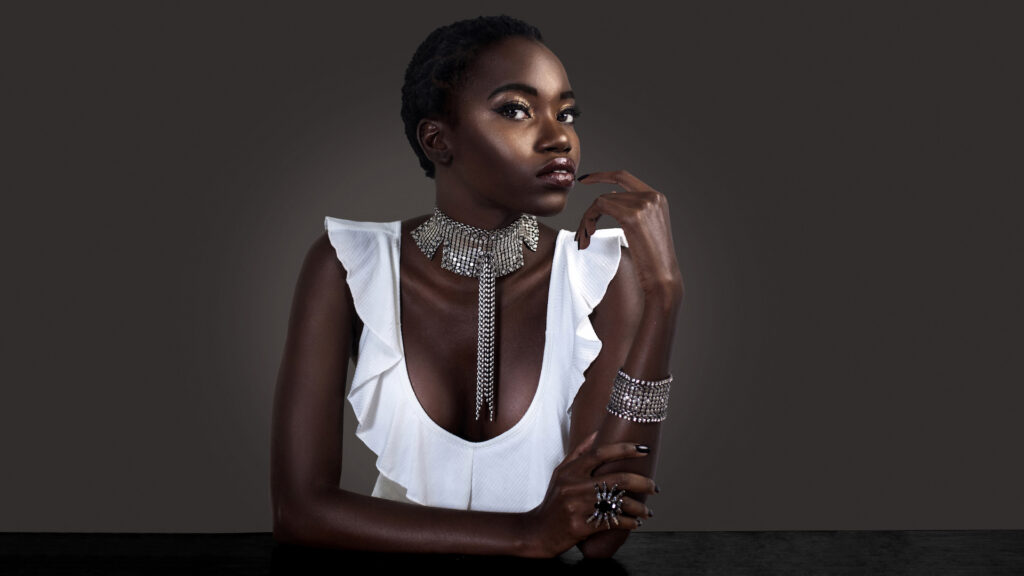 Flirtatious beauty editorial of young Black woman sitting at a bar wearing white sleeveless blouse and silver jewelry.