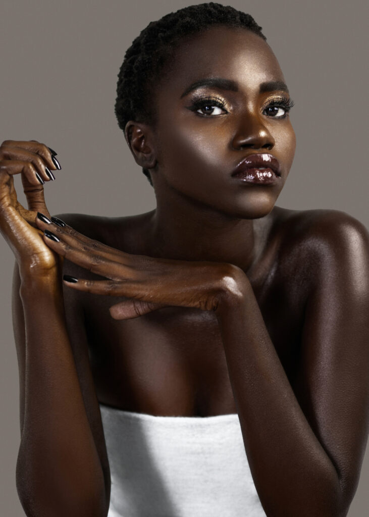 Beauty editorial portrait of young Black woman in white wrap with short hair against gray background.