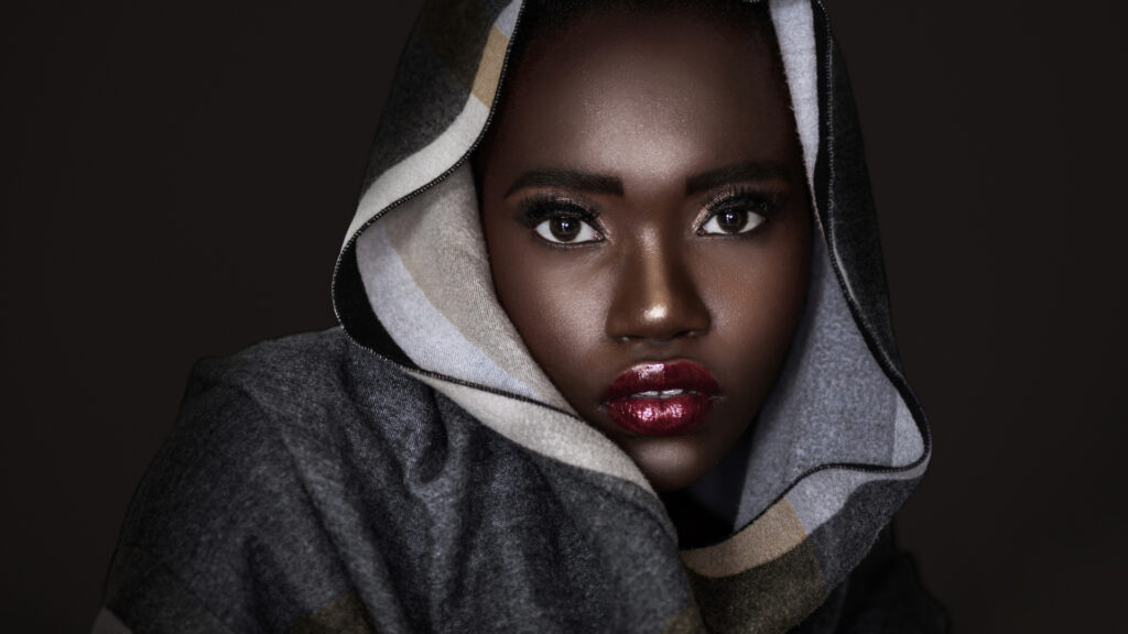 Beauty editorial headshot of young Black woman with curly hair, red lipstick, and colorful headscarf.