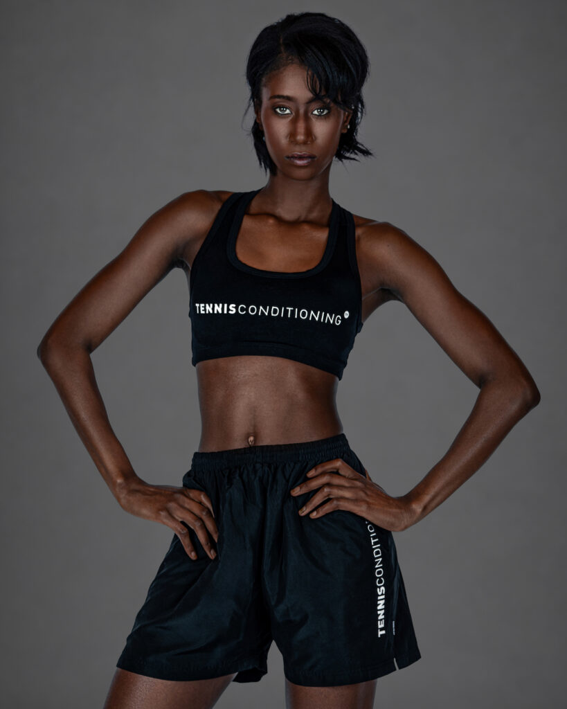 Gigi wearing a black sports bra and black athletic shorts in a confident studio portrait